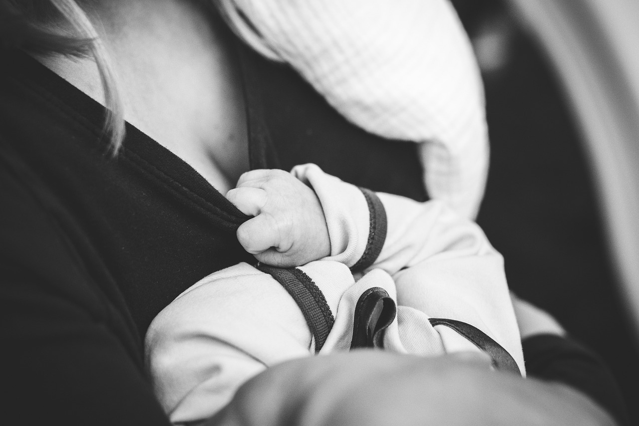 Une mère allaite son bébé au sein, la main du nourrisson posée sur sa poitrine
