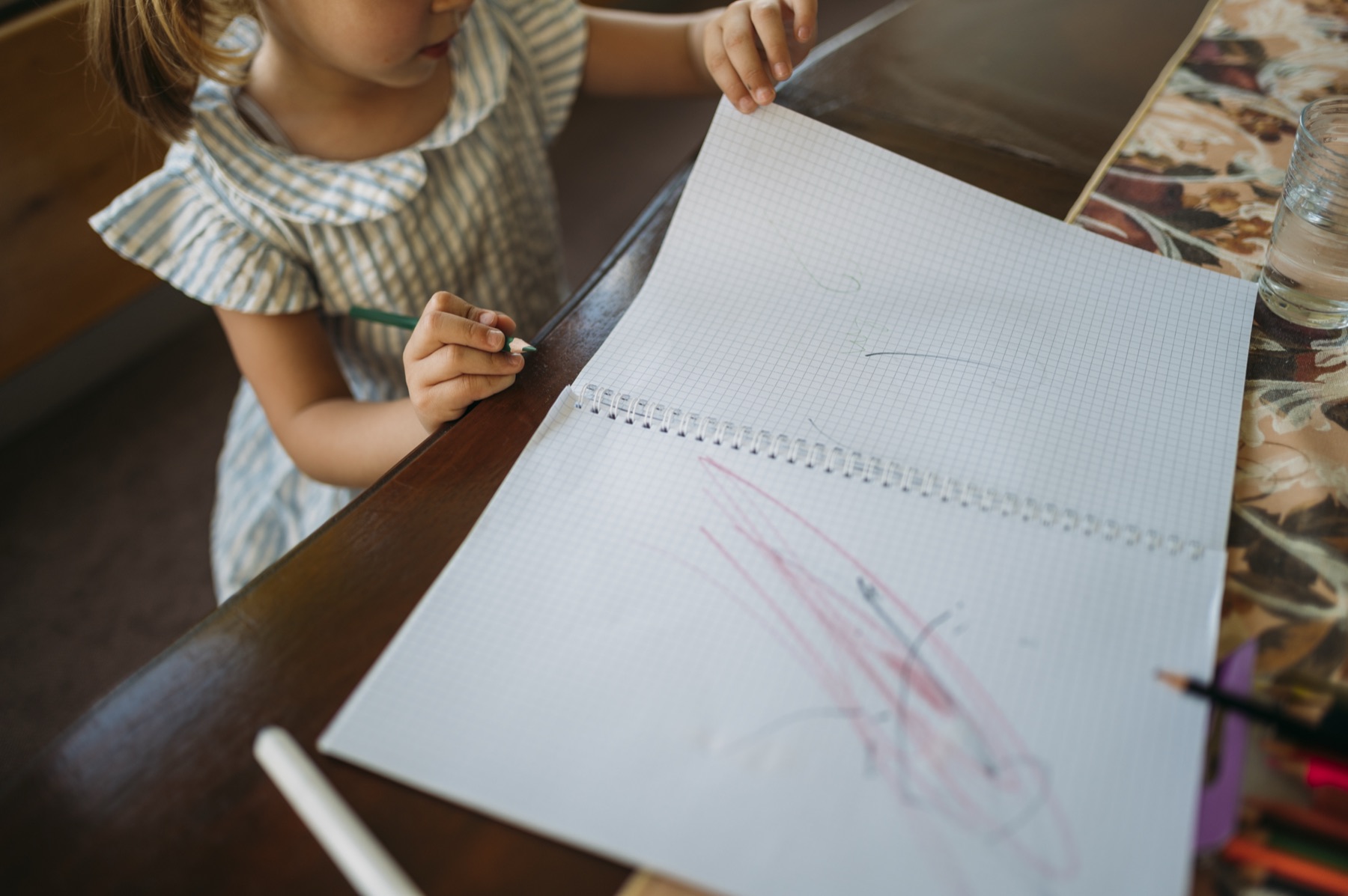 jeune enfant qui trace ses premiers traits au feutre fin sur un carnet à spirale, posé sur une table
