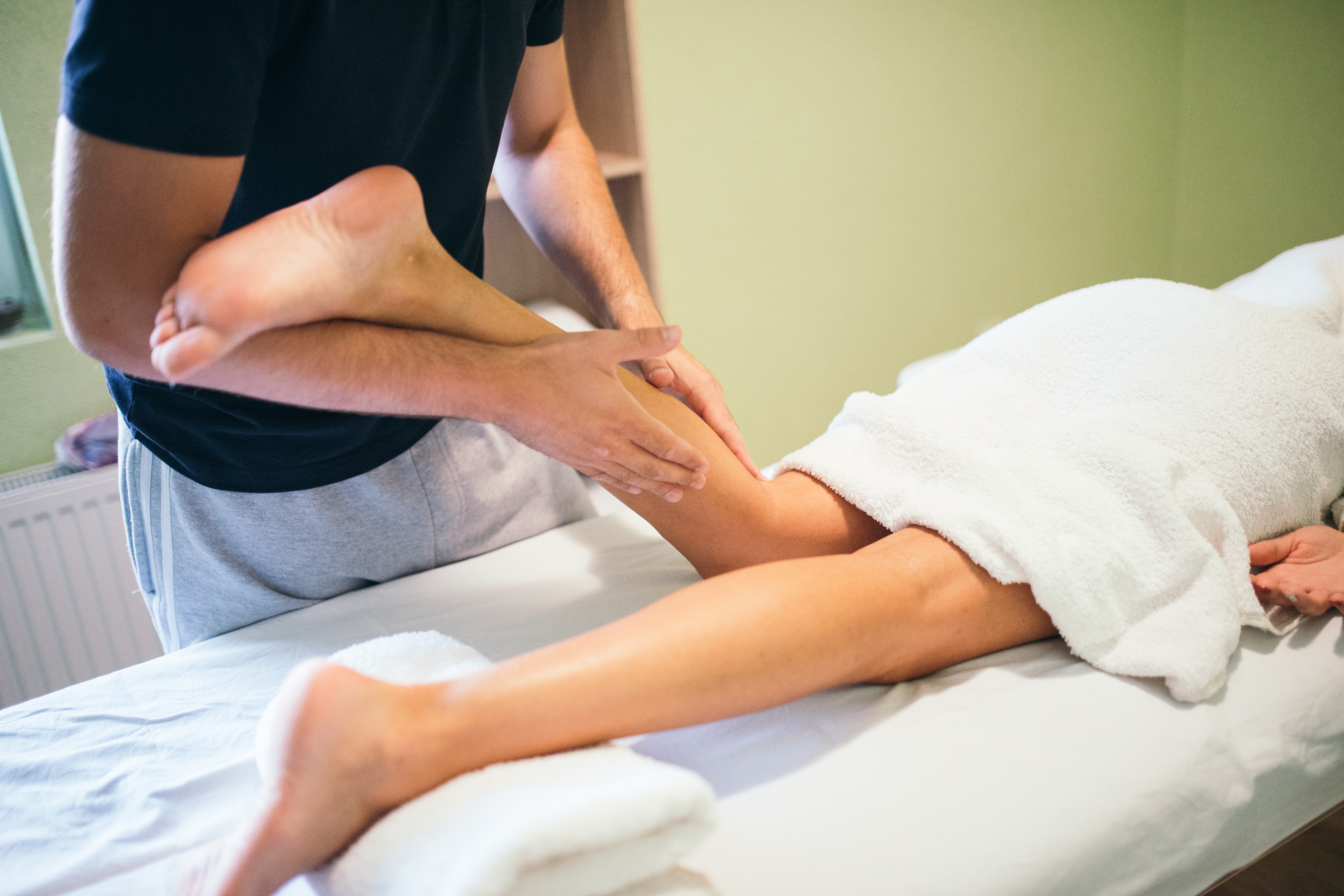 kinésithérapeute manipulant la jambe d'une patiente allongée sur une table de soin, séance de rééducation